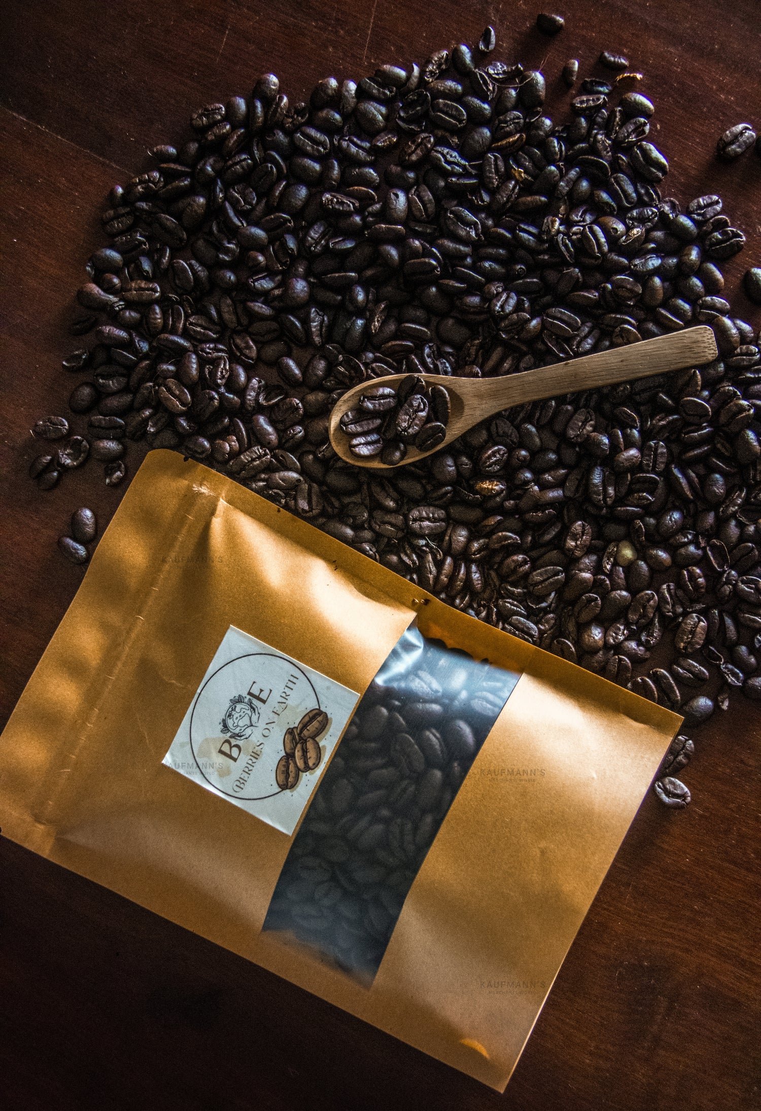Coffee beans with a wooden spoon and a gold coffee bag on a wooden surface