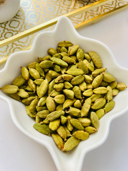 Green cardamom pods in a decorative white bowl on a patterned surface